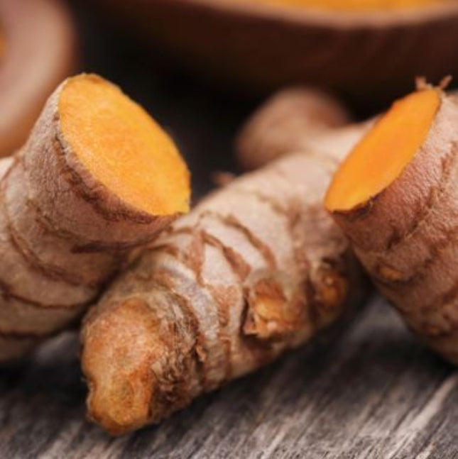 Fresh turmeric root pieces with vibrant orange cross-sections on rustic wood surface