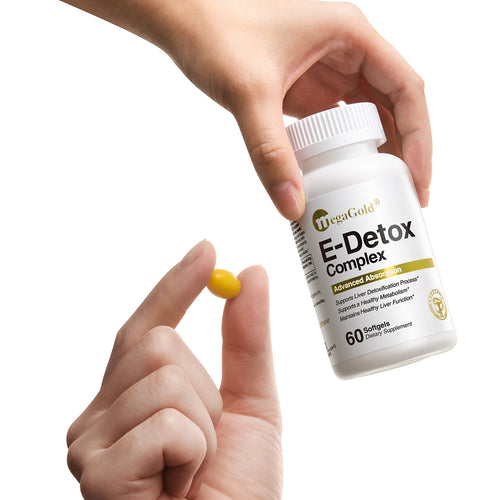 Hand holding MegaGold E-Detox Complex bottle with one yellow softgel capsule pinched between fingers