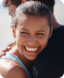 Smiling young woman with slicked-back hair hugging someone outdoors