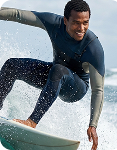 Young man in blue wetsuit surfing a wave, smiling, with ocean spray