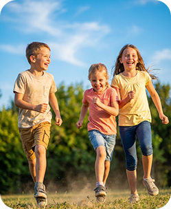 Three joyful children running outdoors on green grass under blue sky