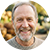 Smiling middle-aged man with gray beard outdoors, warm sunlight, green foliage background
