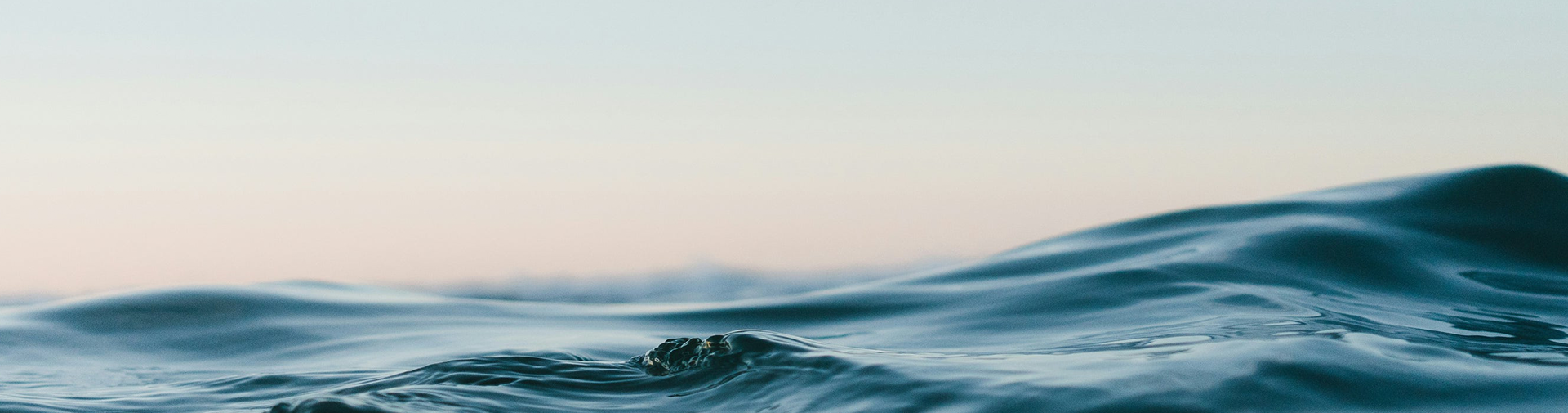 Calm ocean waves at dusk with soft blue water and pastel pink sky on horizon