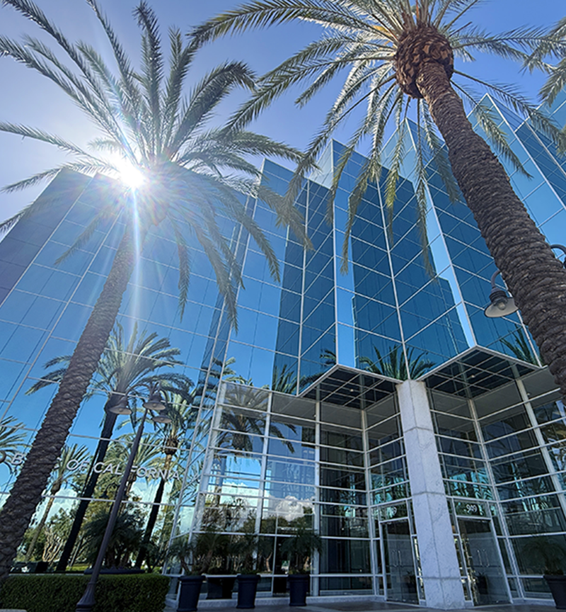 Blue glass office tower with palm trees and bright sunburst, California location